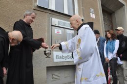 Páter Vojtěch Málek kropí babybox i Zdeňka Juřicu. Já jsem zůstal na suchu.